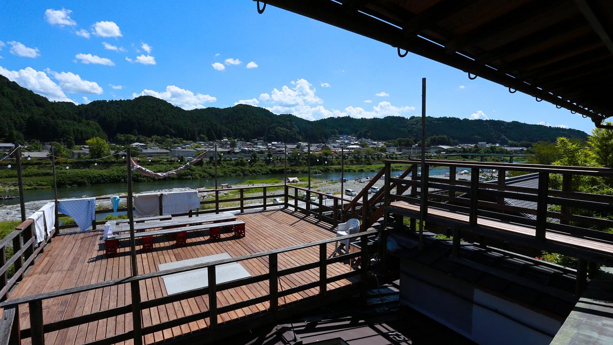 吉野町上市にある三奇楼の屋外の様子。広々としたウッドテラスの奥には吉野川が流れている。よく晴れた空の真下で布団を干している。
