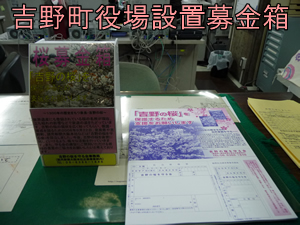 室内で、机の上に、「桜募金箱」と書かれた箱と書類が置かれている写真(吉野町役場設置募金箱)