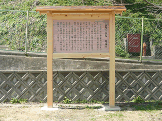 傾斜が迫っているのを防ぐようなフェンスの前に建つ、「吉野山の桜 育成園」と題されその内容が記された、立て札の写真