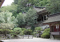 植物がよく手入れされた庭の奥に見える、沢山の木々が伸びている林の中に建つ、古びかしい建物の写真