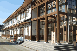 青空の下、「吉野山 桜の学校」と書かれた看板が出入り口にある、沢山の木材が入り組まれて造られている建物の写真