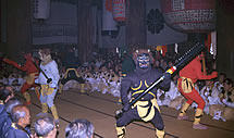 座っている男性たちの前に立つ黒鬼や赤鬼の画像