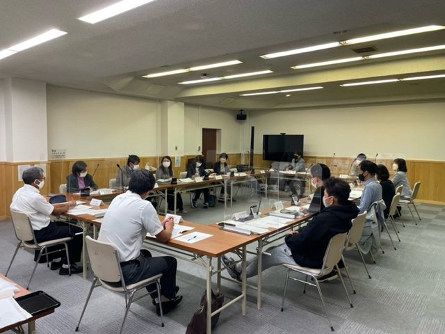 会議室で机を四角く囲むように配置し、沢山の人達が椅子に座り議論している様子の写真