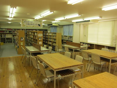 たくさんの本棚と対面式の4人掛けテーブルが並べられている図書室の写真