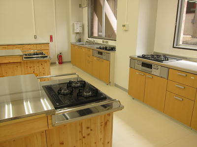 長テーブルの端と調理室壁側にコンロが設置されている調理室内の写真