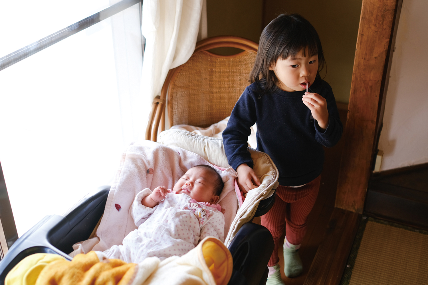 赤ちゃんの横でスティック飴をなめる幼児