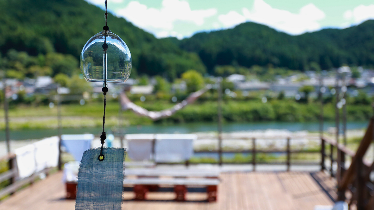 吉野町の空き家を活用したゲストハウスから見た吉野川の風景。手前に風鈴。その奥には洗濯物と吉野川。よく晴れた空の真下で布団を干している。