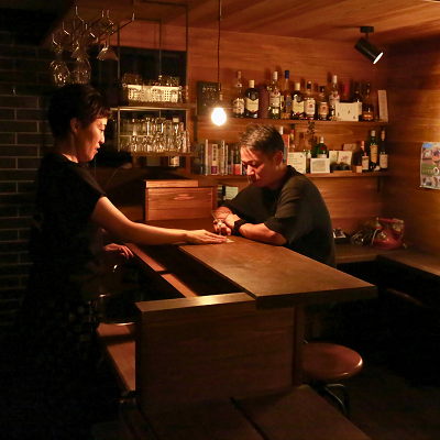 吉野町上市にある三奇楼の倉の室内。バーカウンターに男性が座り、女性がコップを回収している。