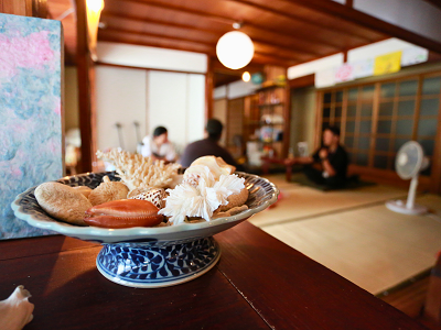 吉野にあるお店屋さんの一コマ。手前には陶器皿の上に貝殻がおいてあり、その奥で話をする3人の様子。
