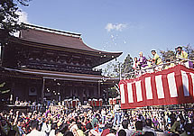 神社の門の前で紅白の幕を張った高台から餅を投げている写真