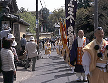 のぼりを持ちながら道路を練り歩く山伏や僧侶の写真