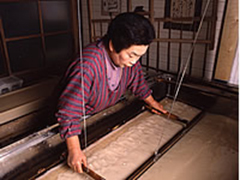 室内で、一人の女性が、茶色の液体を木枠に入れて水で漉いている写真