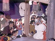 座っている神官の男性を興味深そうに見ている子どもたちの写真