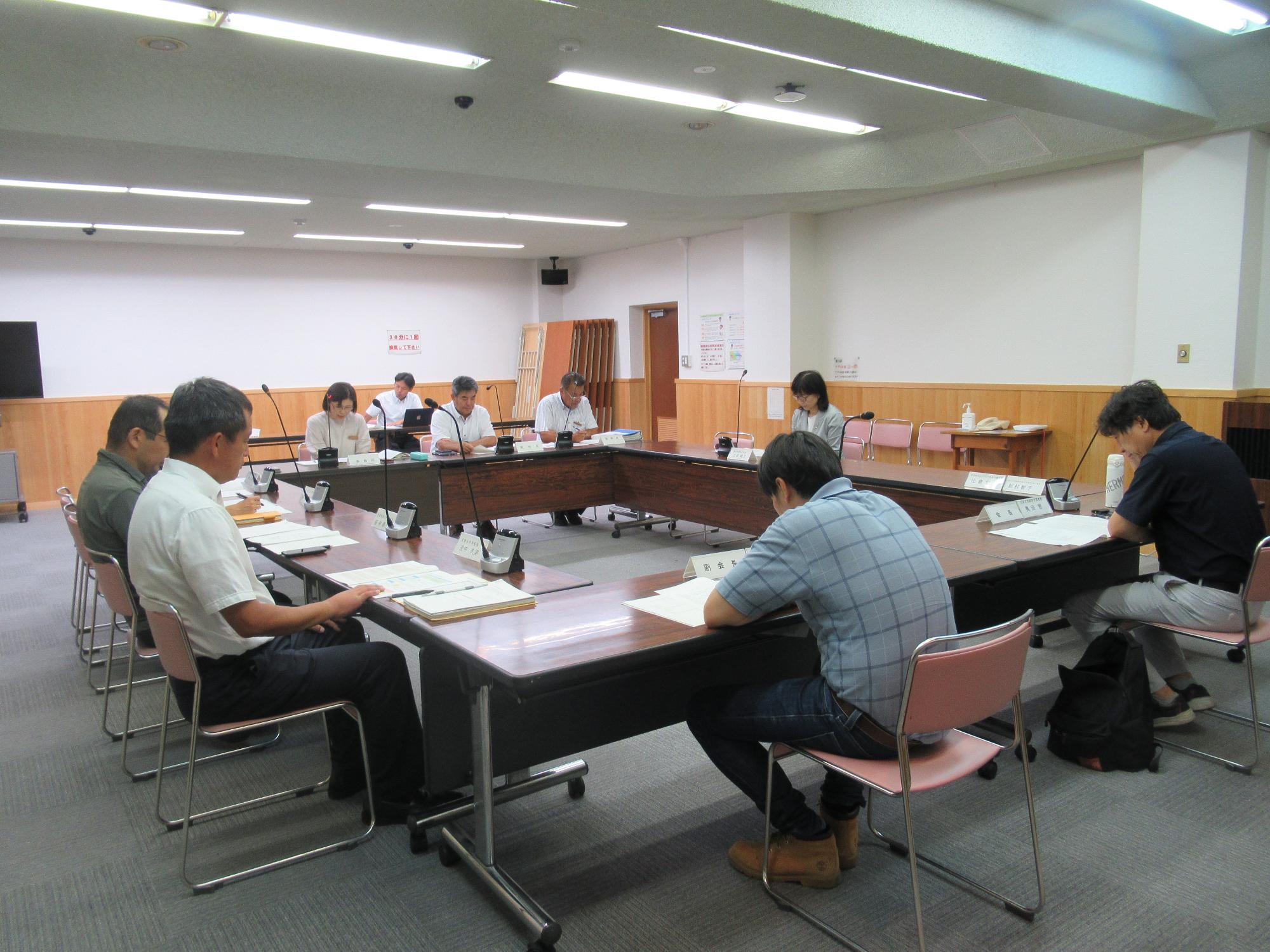 会議室で四角く囲むように配置された机に男性と女性が数名座り、資料を読み込んでいる様子の写真