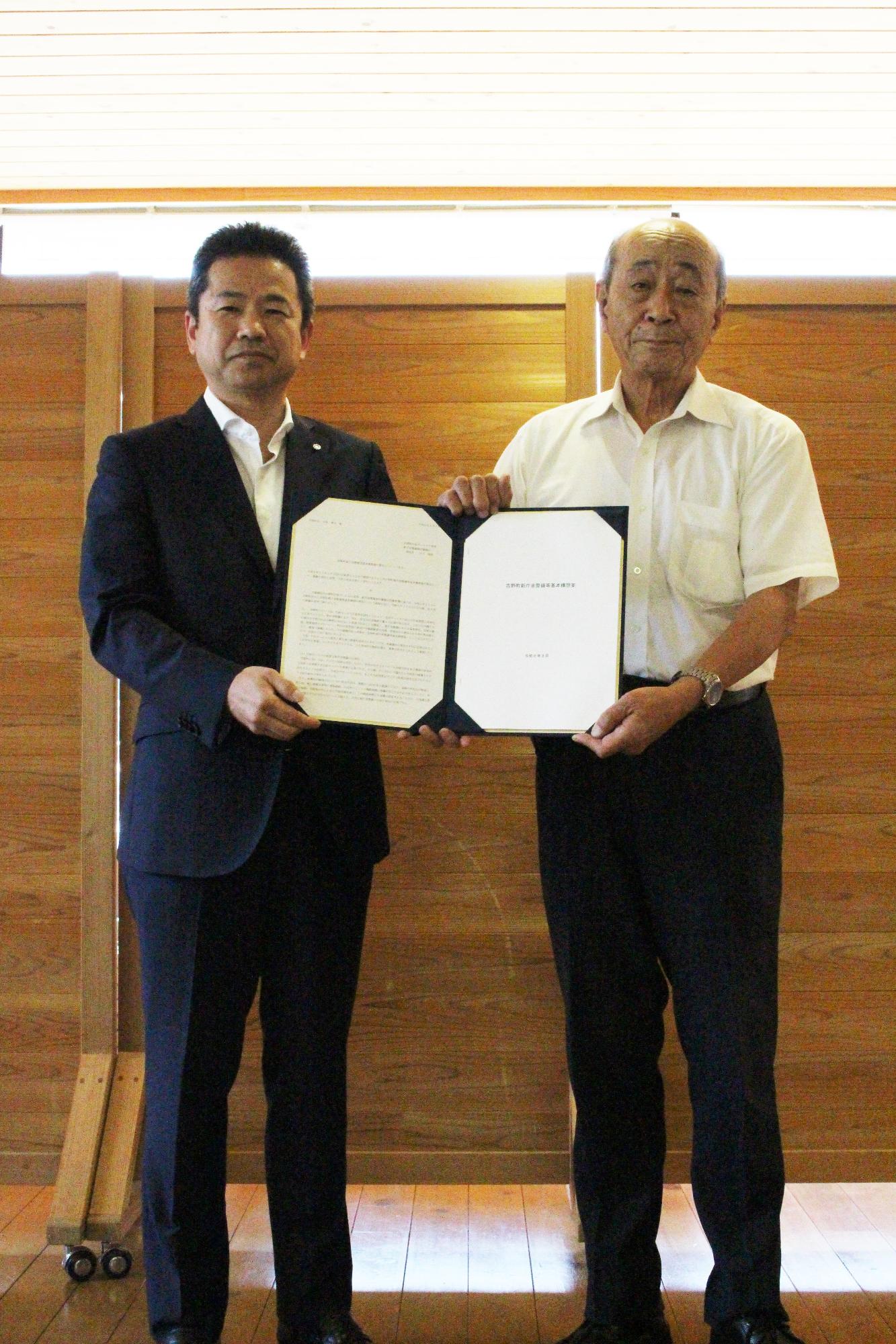 2人の男性が書状を二人でもちこちらを向いている写真