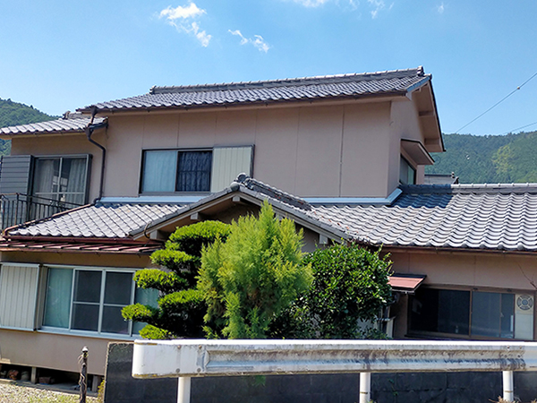 外壁が薄いピンク色、瓦屋根が印象的な2階建ての建物の写真