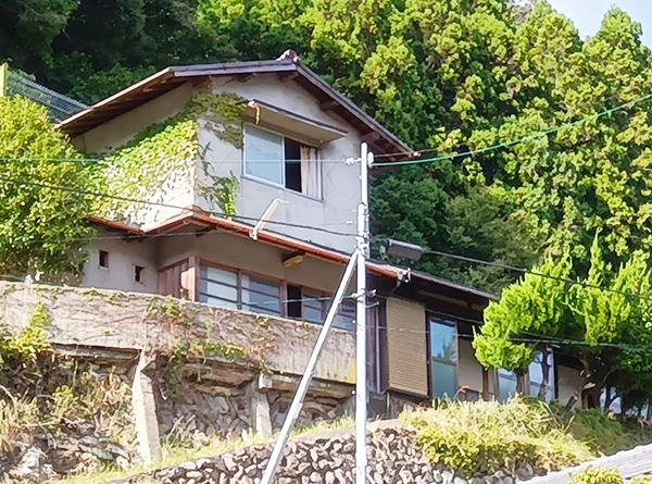 裏には山、石垣の上に建つ白い外壁の2階建ての建物の写真