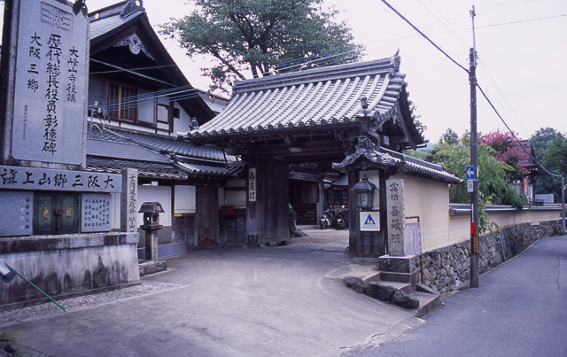 「歴代総長役員彰徳碑」と彫られた巨大な石碑と瓦屋根の門の写真